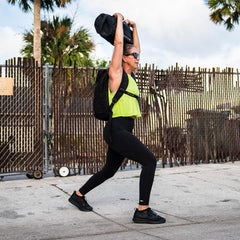 Woman in athletic wear performing lunge while holding black GORUCK bag overhead outdoors