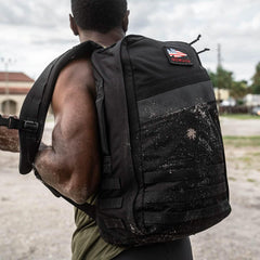 Man outdoors carrying a rugged GORUCK Blackout 25L rucksack with sand on the bag.