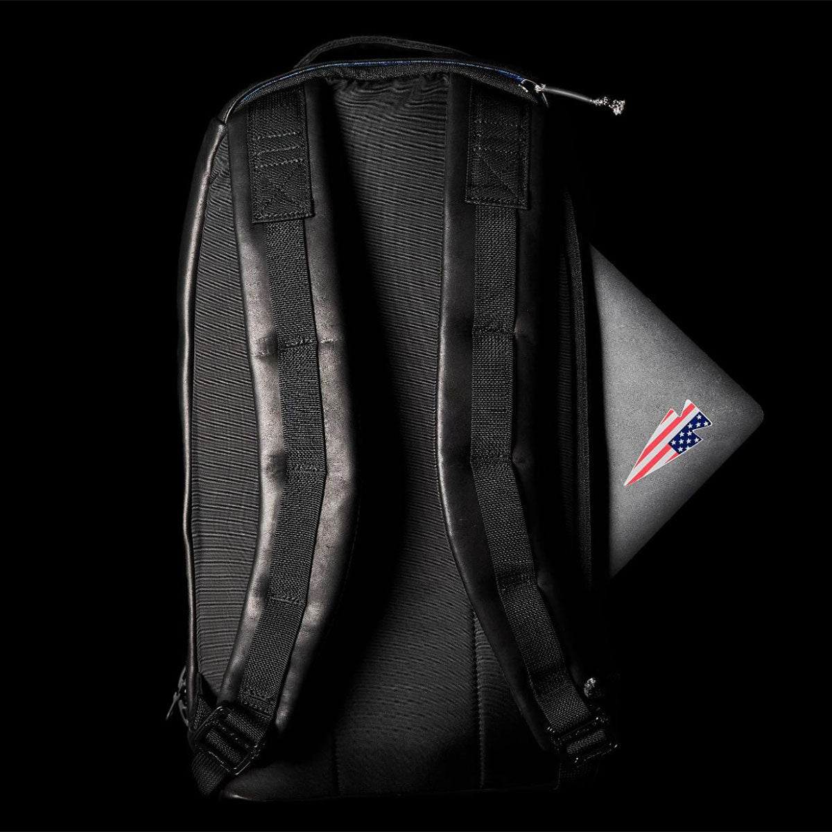 A black backpack with padded straps and a laptop with a USA sticker partially tucked inside.