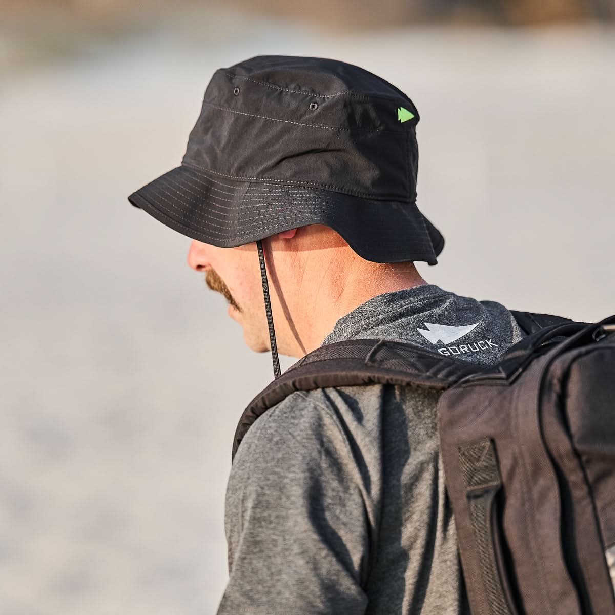 A person wearing a black Boonie Hat - Slick - ToughDry and a backpack, with 