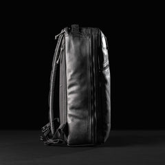 Side profile of a black leather GORUCK Bullet 15L backpack with zippers and shoulder straps on black background