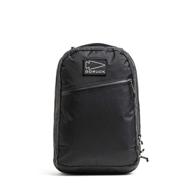 Black Double Compartment Bullet Ruck - XPAC travel backpack with a bombproof laptop compartment, front zipper pocket, and logo patch, set on a plain white background.