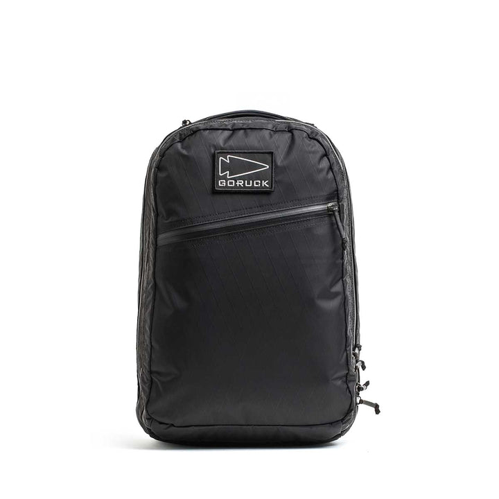 Black Double Compartment Bullet Ruck - XPAC travel backpack with a bombproof laptop compartment, front zipper pocket, and logo patch, set on a plain white background.