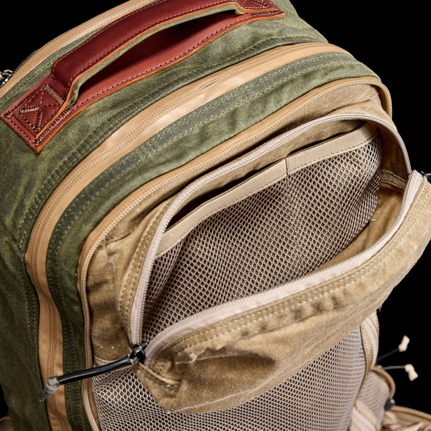 The green and tan Waxed Canvas 18L Bullet Ruck features a mesh front pocket, leather handle, and dual compartment design against a black backdrop. Built to last, it includes the renowned Scars Lifetime Guarantee.