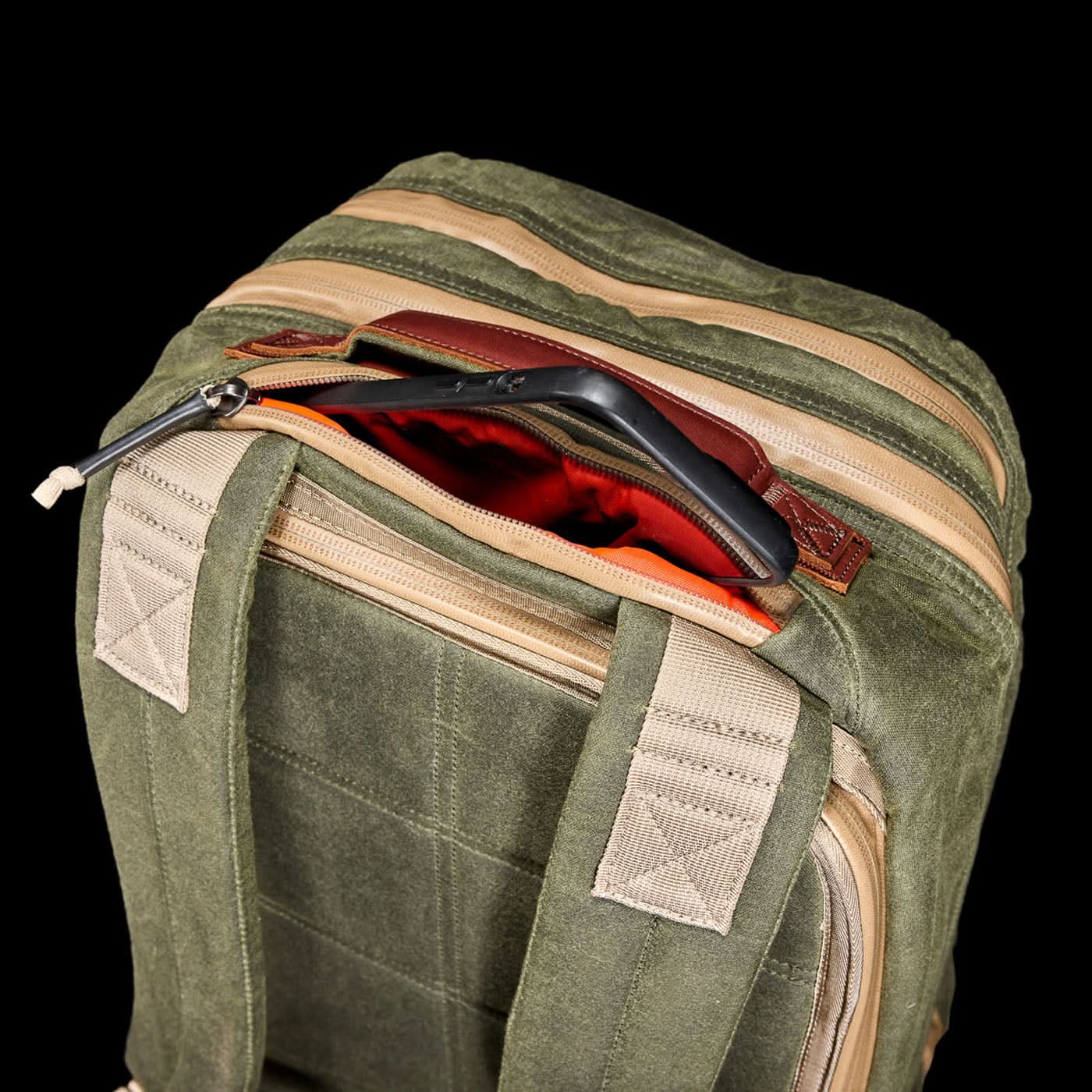 The Waxed Canvas 18L Bullet Ruck boasts tan zippers and a red-lined pocket with a black tablet partially visible. Carry your essentials in style, knowing they're backed by the Scars Lifetime Guarantee.