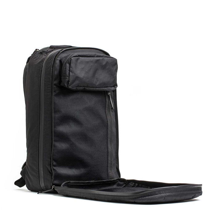 The Double Compartment Bullet Ruck - XPAC stands upright with its front compartment unzipped, revealing mesh pockets. It features a bombproof laptop compartment for ultimate protection while traveling.