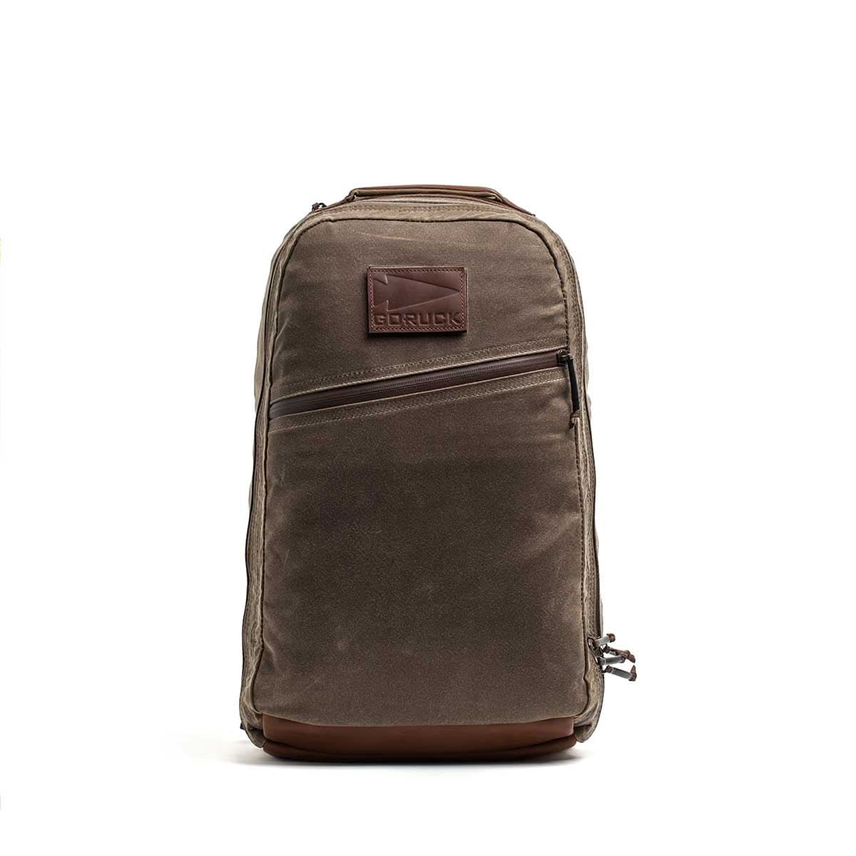 The Waxed Canvas 18L Bullet Ruck features a brown waxed canvas build, front diagonal zipper pocket, leather accents, stitched logo patch, and a rugged dual-compartment design.