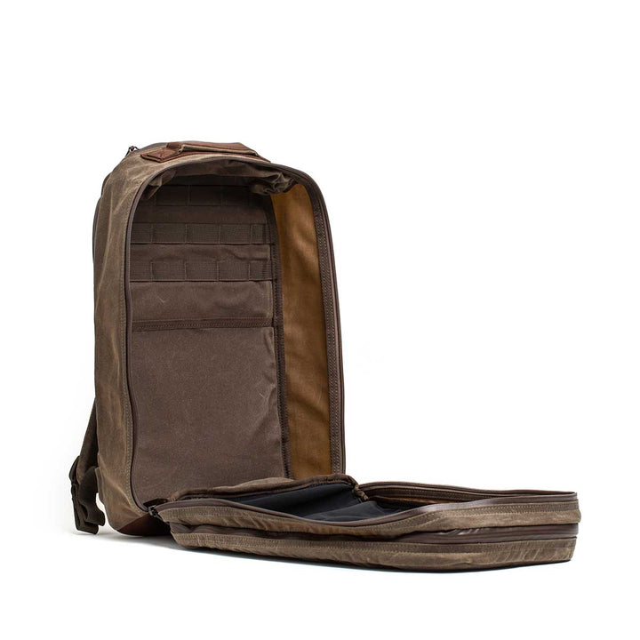 The Waxed Canvas 18L Bullet Ruck stands upright with both compartments unzipped, displaying its neatly organized interior pockets and sections.