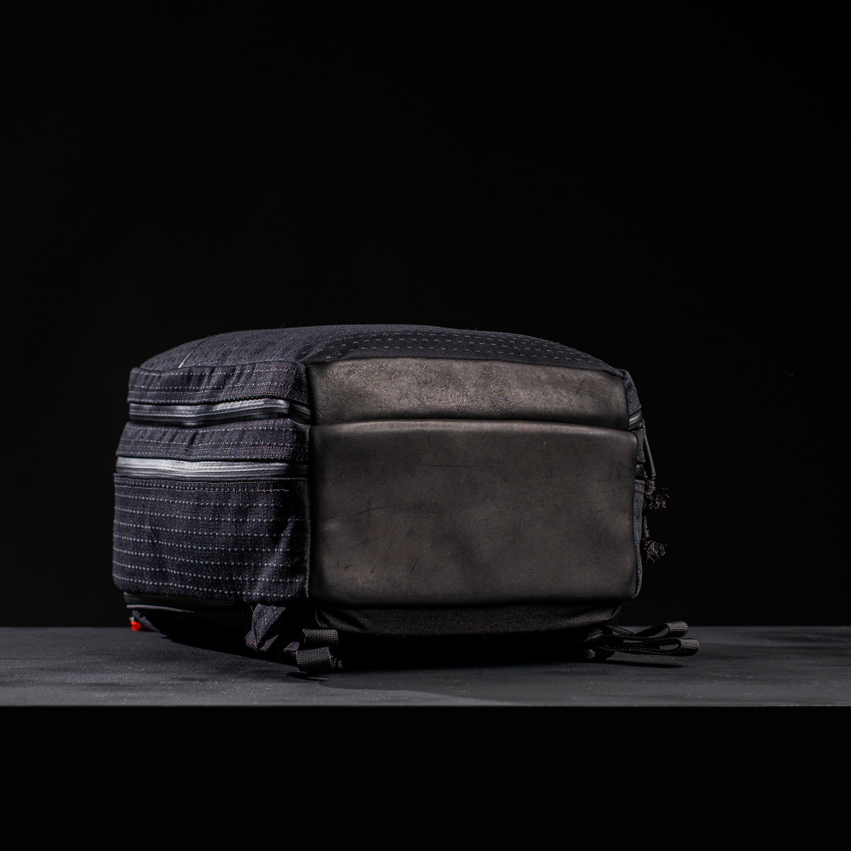 A Bullet Ruck x Carryology - GRXC2 Samurai 2.0 backpack rests flat on its sturdy base against a dark backdrop, highlighting the exclusive JPXDP 17oz Black Samurai Sashiko design.