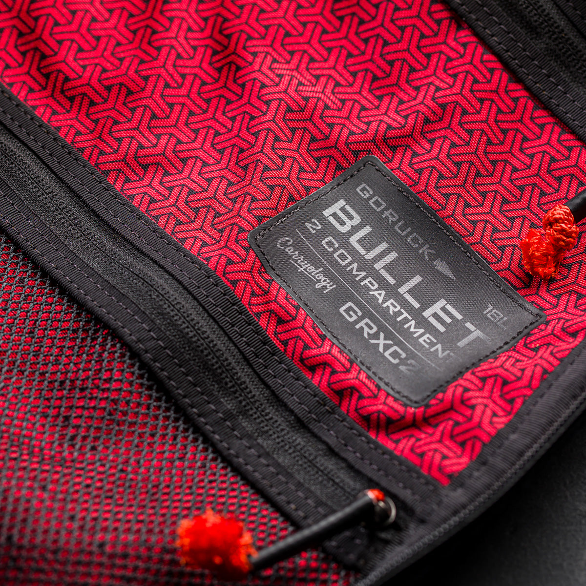 Close-up of a red and black Bullet Ruck x Carryology - GRXC2 Samurai 2.0 label, showing two compartments and zipper pulls on this limited-edition backpack inspired by the JPXDP 17oz Black Samurai Sashiko design.
