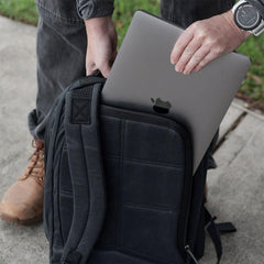 Person placing silver MacBook laptop into black GORUCK backpack outside on sidewalk
