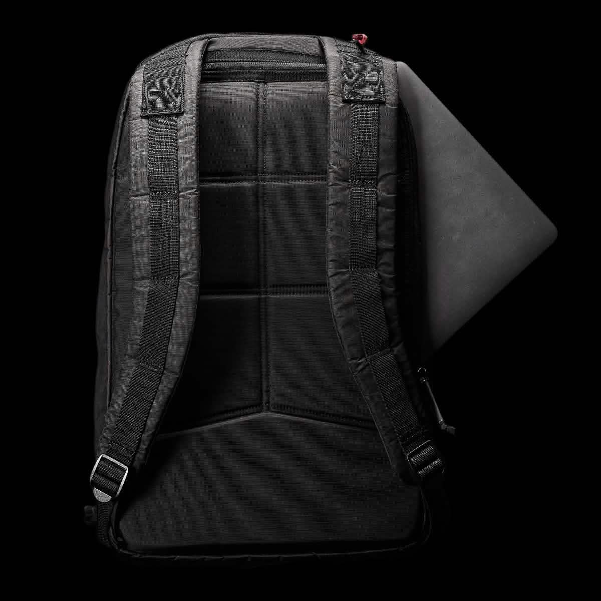 A Bullet Ruck Double Compartment - Dyneema backpack from GORUCK, featuring a black design with padded straps, is displayed on a dark background. A laptop can be seen snugly fitted into the top compartment of the bag. The back panel showcases a grid pattern for enhanced support and comfort, crafted from durable Dyneema material that comes with a lifetime guarantee.