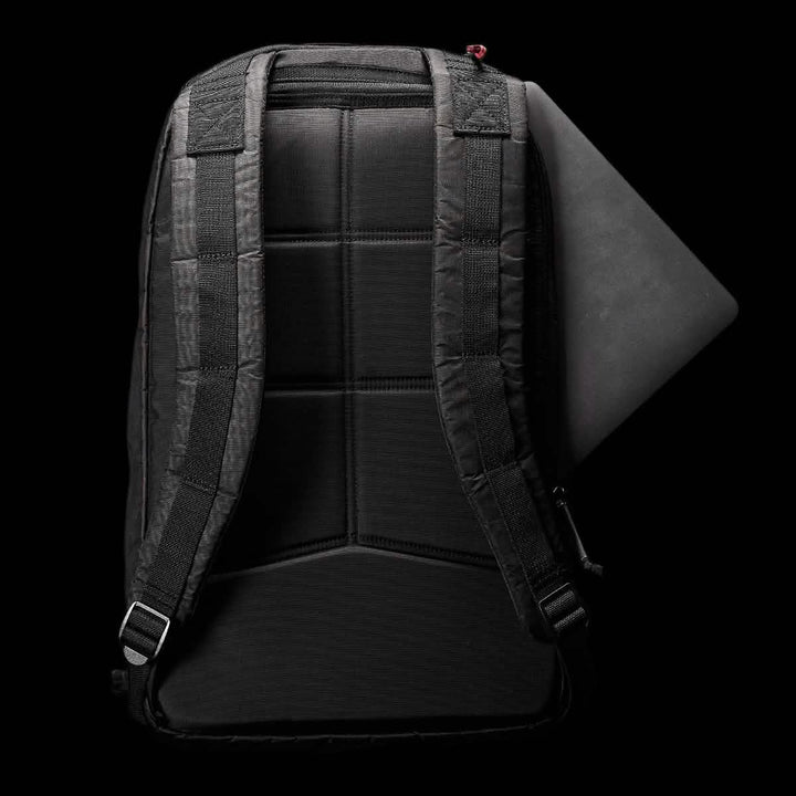 A Bullet Ruck Double Compartment - Dyneema backpack from GORUCK, featuring a black design with padded straps, is displayed on a dark background. A laptop can be seen snugly fitted into the top compartment of the bag. The back panel showcases a grid pattern for enhanced support and comfort, crafted from durable Dyneema material that comes with a lifetime guarantee.