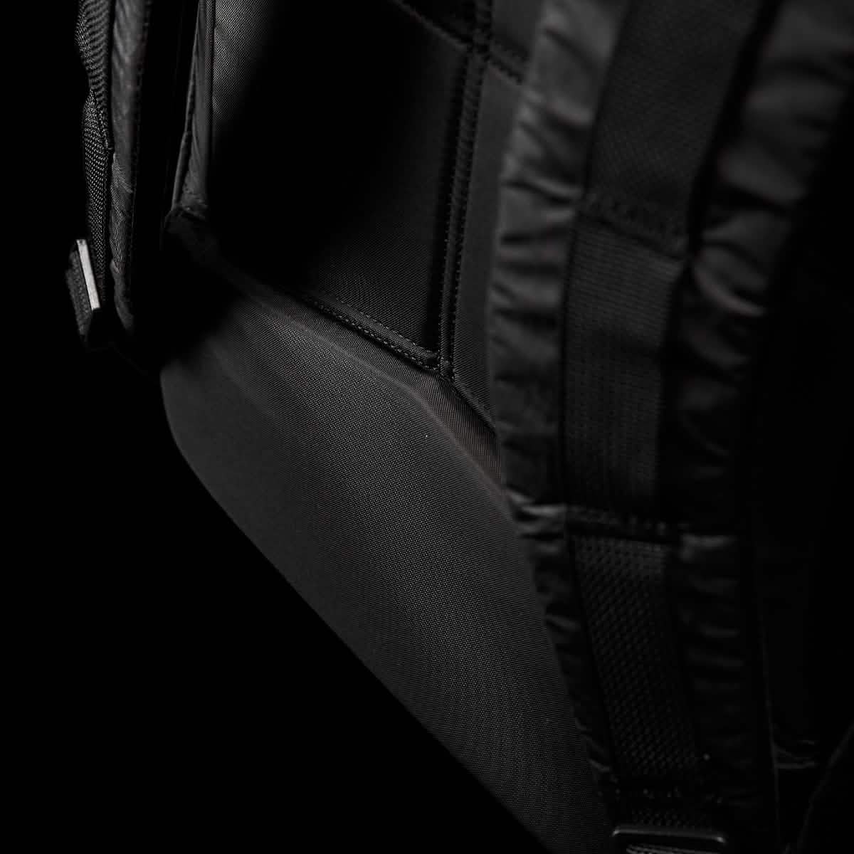Close-up image of a black Bullet Ruck Double Compartment backpack by GORUCK, emphasizing the shoulder strap area with detailed stitching and a padded section. The dark backdrop accentuates the texture and design of the durable Dyneema fabric, which is backed by a lifetime guarantee.