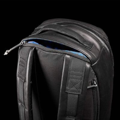 Close-up of a GORUCK Bullet Ruck x Carryology - Berserker Viking on a white background, showcasing two padded shoulder straps and robust zippers. The top of the backpack is slightly open, revealing a hint of the blue interior lining, indicating its rugged GRXC program design.