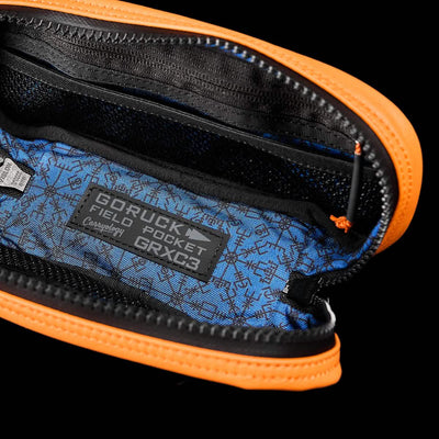Open view of the Echo Field Pocket x Carryology - Berserker Viking, an orange pouch with a black zipper that reflects the resilience of a Viking shield. Inside, the blue lining evokes the Nordic seas and displays a label reading GORUCK. The berserker-inspired compartments exhibit organizational prowess in patterned fabric.