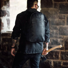 Man wearing black rugged backpack inside stone building holding an axe, showcasing tough rucking gear