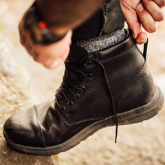 Person tying laces on durable black GORUCK leather rucking boots with gray socks