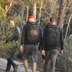 Three men hiking in a forest wearing water-resistant black backpacks and rugged outdoor clothing