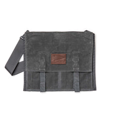 The Waxed Canvas Claymore Sling Bag features a dark gray waxed canvas, a shoulder strap, and a brown leather patch on the front flap for a modern, versatile style.