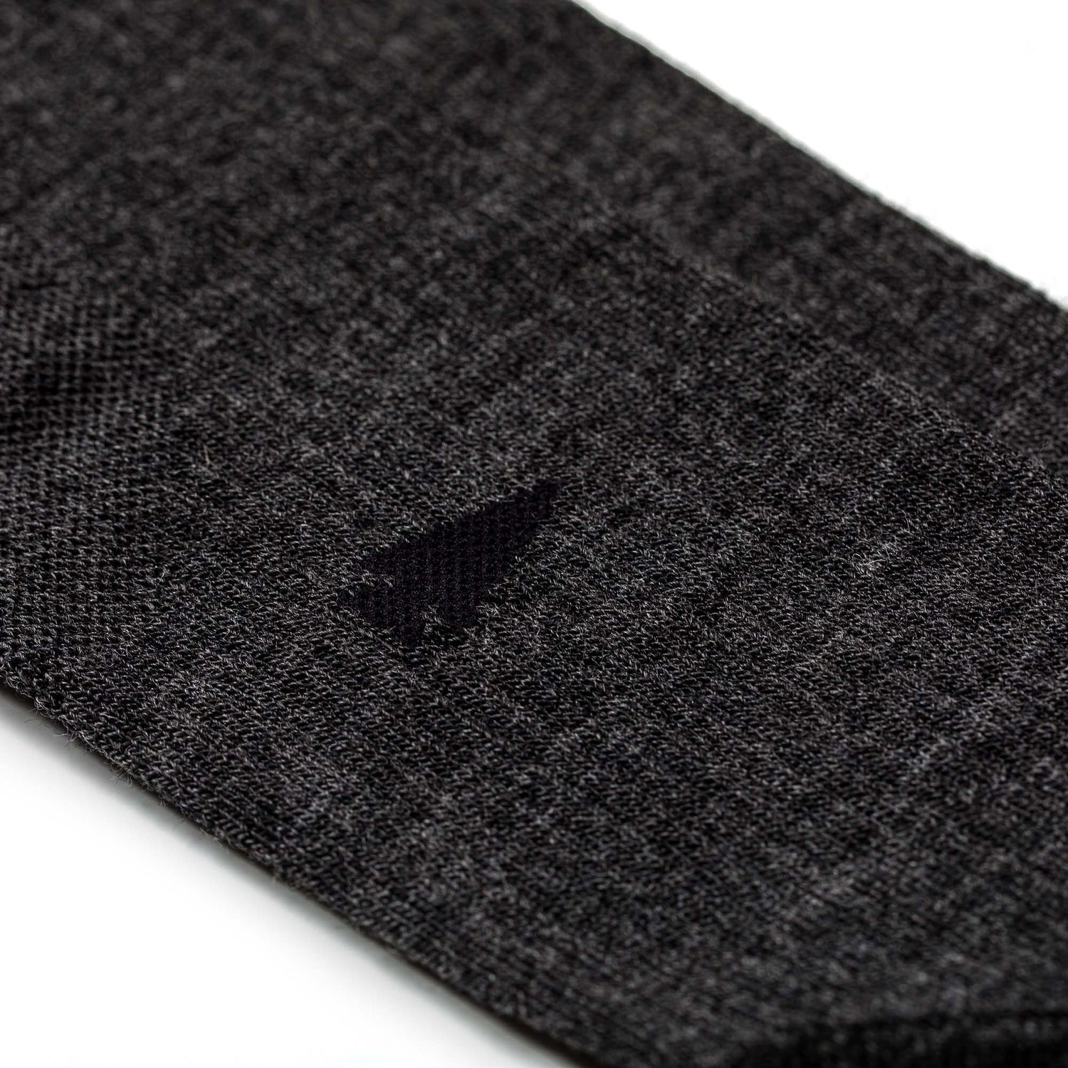 Close-up of a small hole in a dark gray Merino Compression Sock against a white background.