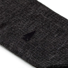 Close-up of a small hole in a dark gray Merino Compression Sock against a white background.