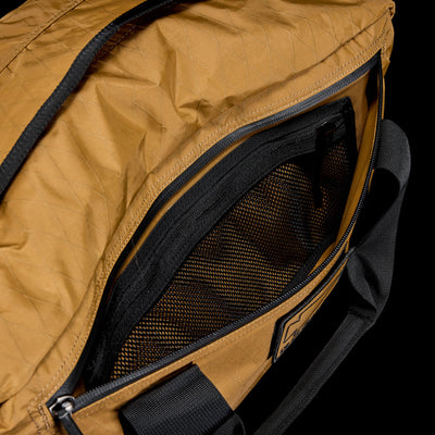 Close-up of an open Kit Bag - X-PAC, crafted from X-PAC VX21 material, featuring mesh and zippered inner pockets and a black shoulder strap.