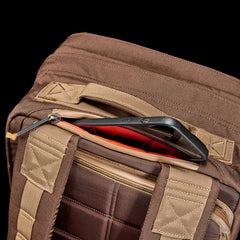 A smartphone partially sticks out of a zippered pocket on the GR2 - Ballistic Nylon Cordura ruck travel bag, set against a black background.