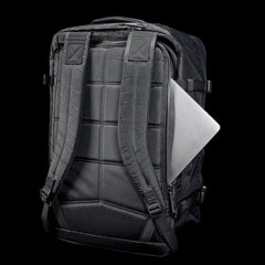 The GR3 - X-PAC, a black waterproof carry-on backpack, features a silver laptop partially tucked into its back pocket, shown against a black background.