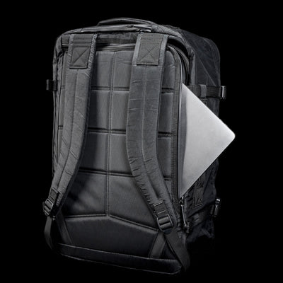 The GR3 - X-PAC, a black waterproof carry-on backpack, features a silver laptop partially tucked into its back pocket, shown against a black background.