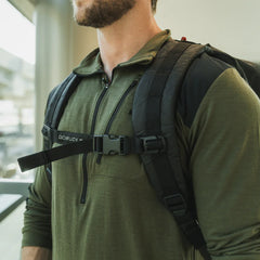 Close-up of man wearing olive green quarter-zip pullover and black GORUCK backpack with chest strap indoors