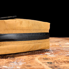 Close-up of the GR2 Field Pocket - X-PAC, a tan fabric bag with an AquaGuard zipper, resting on a worn wooden surface against a black background.