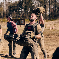 Three men, looking focused and determined, lift heavy sandbags outdoors during a fitness challenge with the Rucker 5.0 as they test their strength and endurance through rucking.