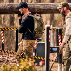 Two men in abrasion resistant ToughDry pants walk outdoors while carrying a heavy wooden log on their shoulders.