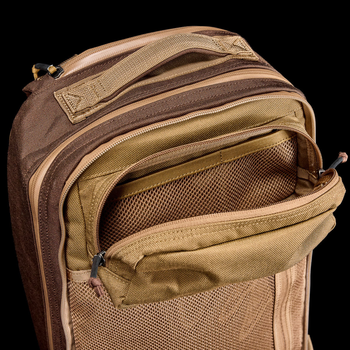 Tan and brown Double Bullet Ruck (18L) with a zippered front pocket open, showing mesh interior and bombproof laptop compartment, on a black background.