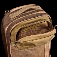 Tan and brown Double Bullet Ruck (18L) with a zippered front pocket open, showing mesh interior and bombproof laptop compartment, on a black background.