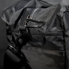 Close-up of the Kit Bag - X-PAC in black, crafted from X-PAC VX21 nylon with a zipper, strap, and metal clasp, set against a dark background.