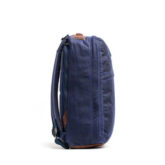 The GR1 USA - Heritage Waxed Canvas backpack is shown from the side with shoulder straps and a zipper, made from durable materials, and displayed against a white background.