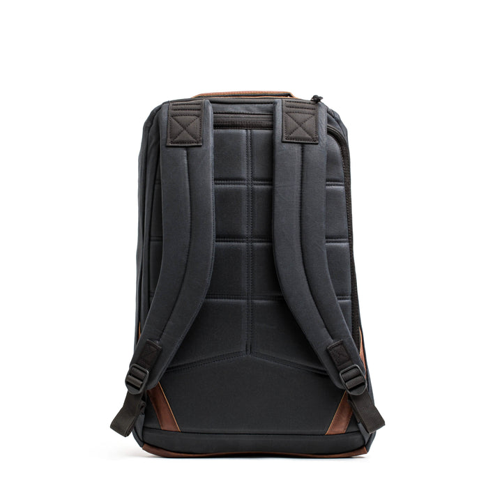 A front view of the GR1 USA - Heritage rucksack by GORUCK, showcasing a black design with brown accents, including padded straps and a quilted back panel. Made from waxed duck canvas, it stands upright against a white background, offering a blend of retro charm and modern functionality.