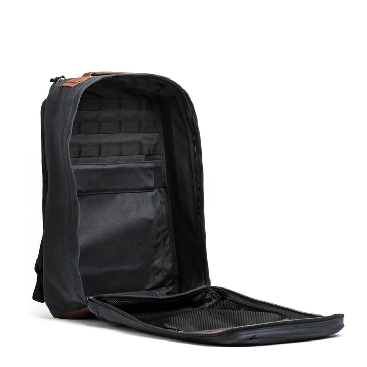 A sleek black GR1 USA - Heritage backpack by GORUCK features a partially open front zipper that reveals multiple compartments and pockets, with an interior design reminiscent of a classic rucksack. It includes a padded laptop compartment and additional sections for organization.