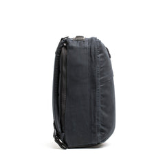 Side view of the GORUCK GR1 USA - Heritage, a black rectangular laptop bag featuring a shoulder strap and zipper pockets. This sleek and compact retro canvas rucksack is designed for convenient portability and storage of electronic devices.