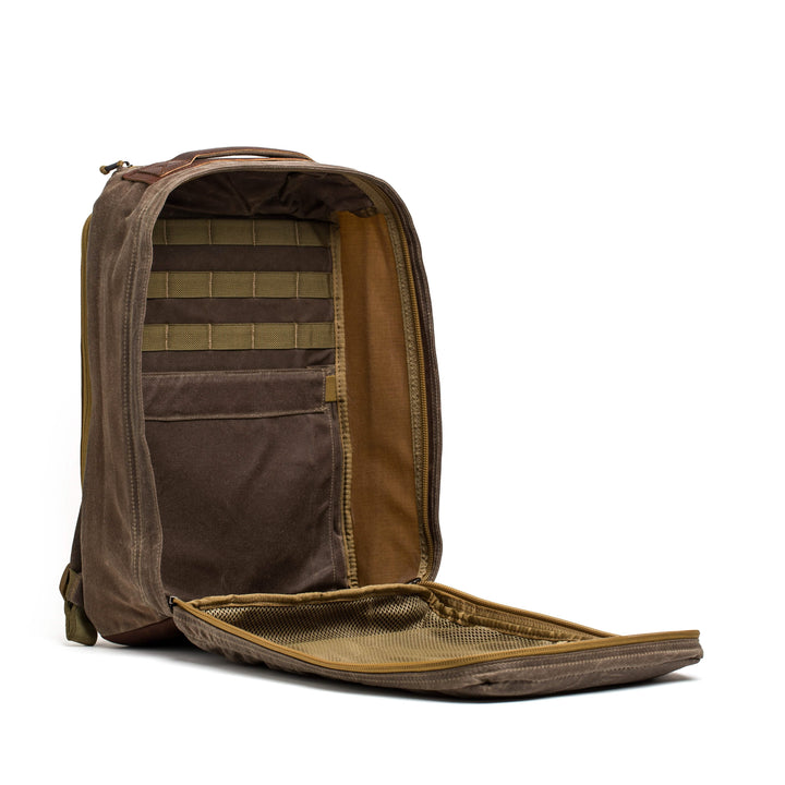 The GR1 USA - Heritage by GORUCK showcases a spacious interior. On the left side, several fabric loops efficiently organize small items. The front flap uncovers an additional mesh pocket for extra storage. Made from robust waxed canvas, it is presented against a simple white background.