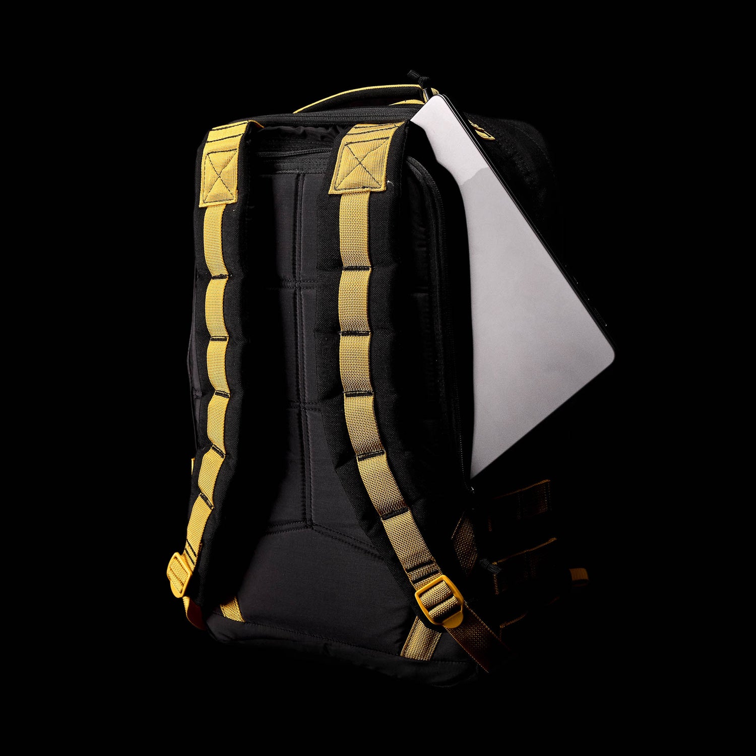 A black GR1 rucksack featuring yellow straps and a partially visible laptop, crafted from Special Forces grade materials, set against a black background.