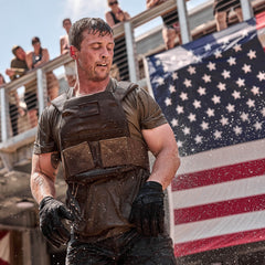 A man in wet tactical gear stands in front of a U.S. flag with water splashing around him, demonstrating the durability and comfort of our Slick Short Sleeve Tee - Tri-BlendX.
