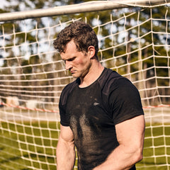 A man wearing the Men’s Commando Tee - Merino Wool stands in front of a soccer goal, looking down seriously.