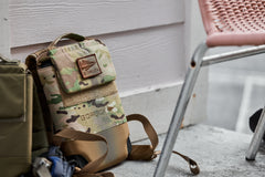 A camouflage GORUCK backpack rests on the ground by a metal chair, next to the RPC 3.0 + 10lb Ruck Sandplate designed for weighted training.
