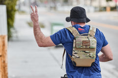 Man wearing a bucket hat and carrying the RPC 3.0 + 10lb Ruck Sandplate backpack flashes a peace sign while walking down the street.