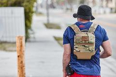 An individual wearing a black hat walks on a city sidewalk with the RPC 3.0 backpack, weighted by a 10lb Ruck Sandplate.