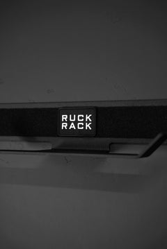 The Ruck Rack® Delta is a heavy-duty black wall-mounted storage solution featuring the “RUCK RACK” label in bold white lettering, ideal for organizing rucks, weight vests, and tactical gear.