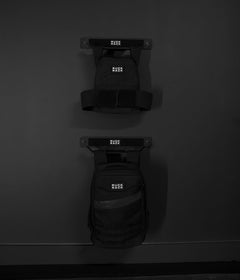 Two black backpacks labeled “Ruck Pack” hang on a sleek, dark grey Ruck Rack® Delta—an ideal heavy-duty wall mount storage solution for rucks, weight vests, and tactical gear.